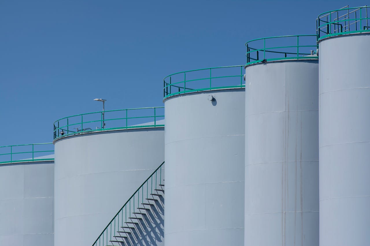 Services-01 Large industrial storage tanks with green railings against a clear blue sky.